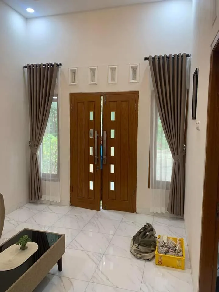 Gorden smokring warna taupe pada dua jendela sempit di kiri dan kanan pintu utama kayu di ruang tamu rumah modern