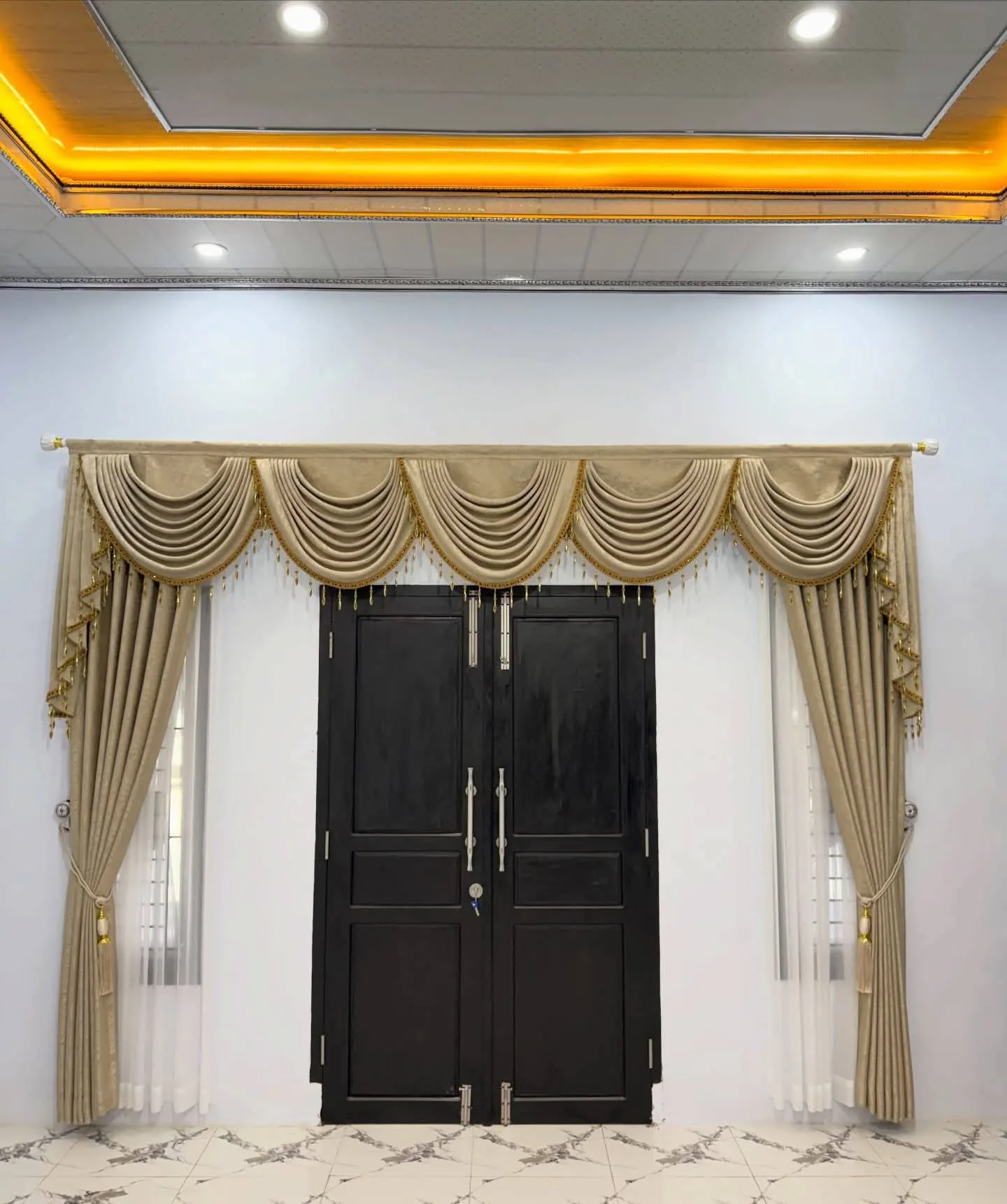 Gorden poni swag warna emas di atas pintu utama kayu hitam, dengan vitrase putih di kedua sisi pintu