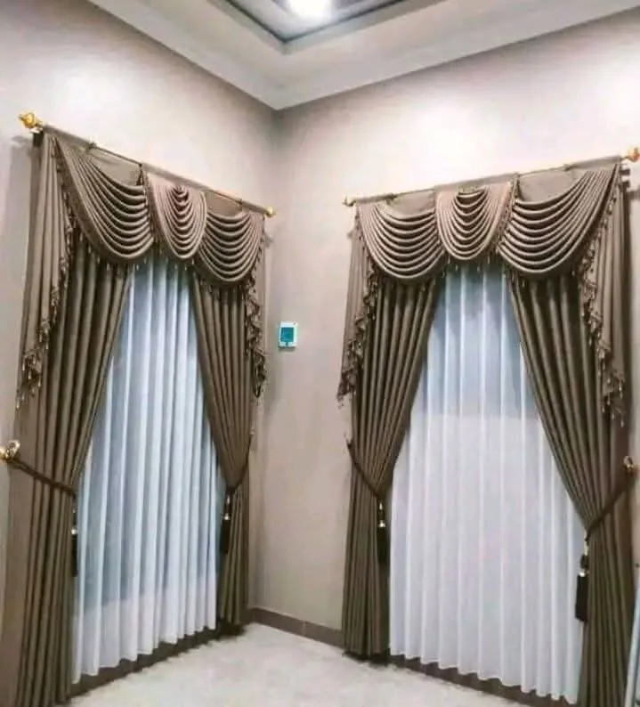 Dua jendela berdampingan dengan gorden poni klasik cokelat keemasan dan vitrase putih, relnya dipasang di atas kusen