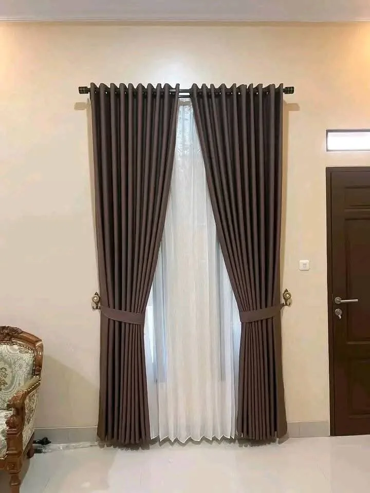 Gorden smokring cokelat tua dengan vitrase putih pada pipa rel hitam berujung finial di dinding krem dekat pintu kayu