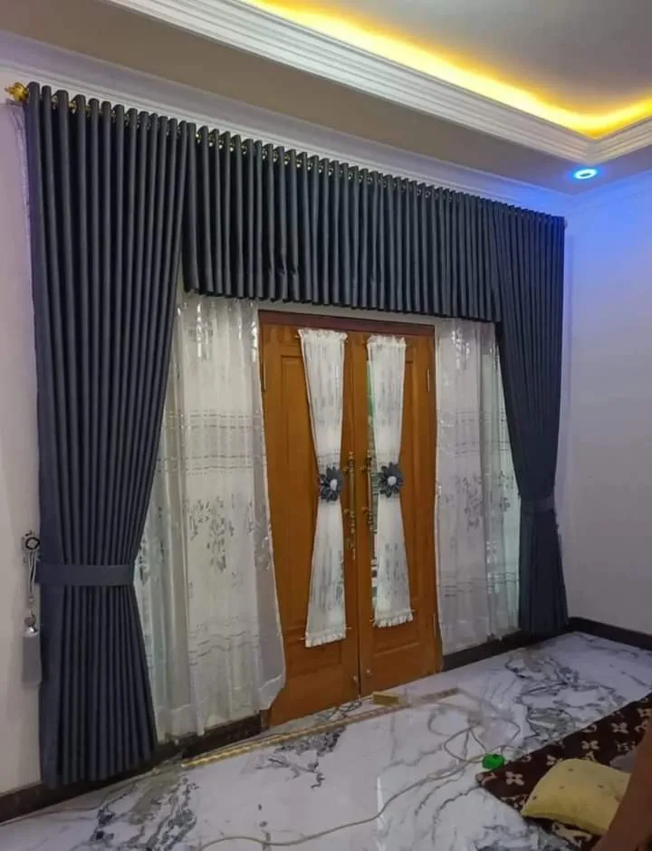 Vitrase bermotif bordir di pintu kayu berkaca, diapit gorden abu-abu tua dengan poni lipit di bagian atas